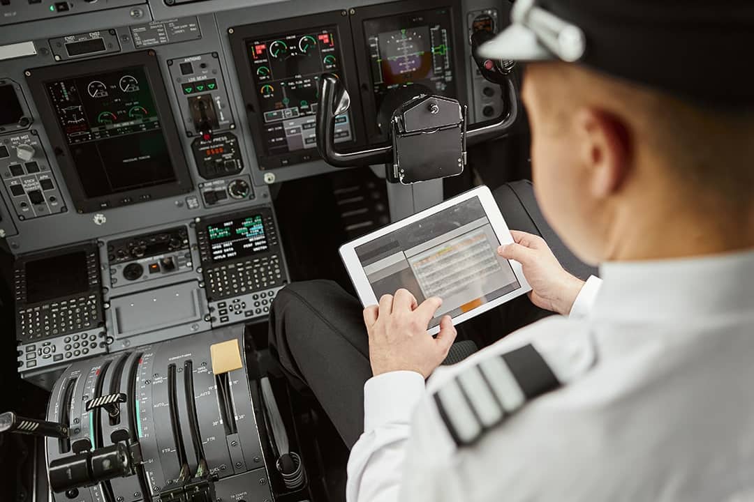 A pilot using a digital display tablet inside the cockpit before an airplane's departure flight.
